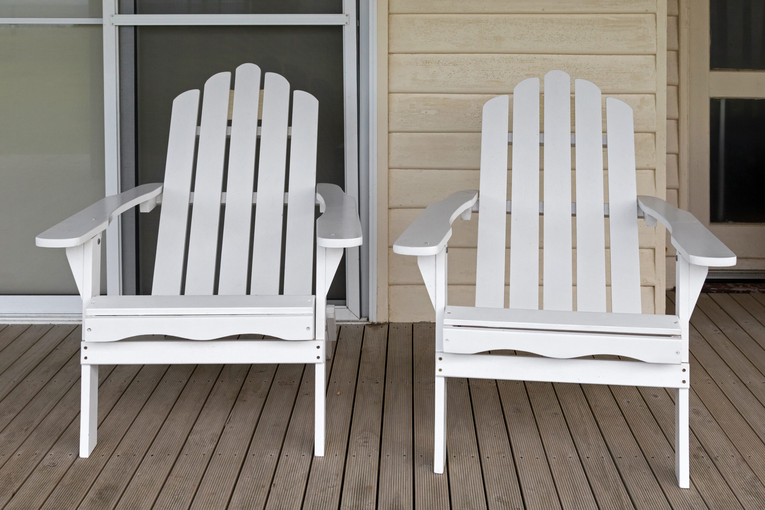 Two white wooden adirondack chair on old weathered front porch